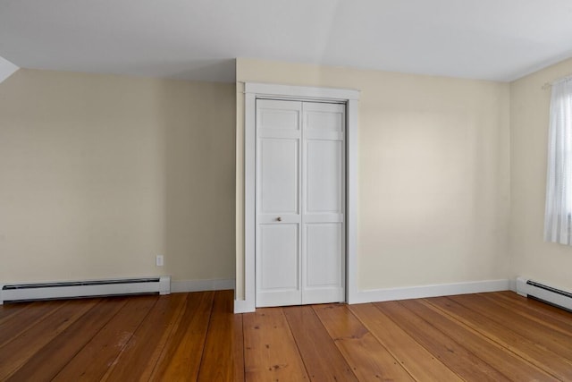 unfurnished bedroom featuring a baseboard heating unit, hardwood / wood-style flooring, and a closet