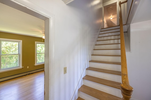 stairs with baseboard heating, hardwood / wood-style floors, and ceiling fan