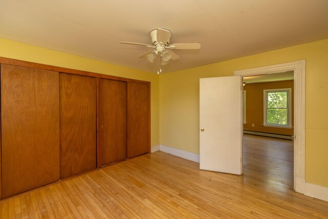 unfurnished bedroom with a closet, ceiling fan, baseboard heating, and light hardwood / wood-style floors