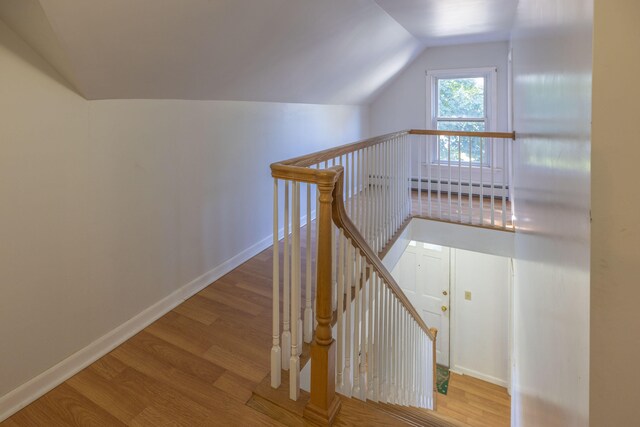 staircase with baseboard heating, vaulted ceiling, and wood-type flooring