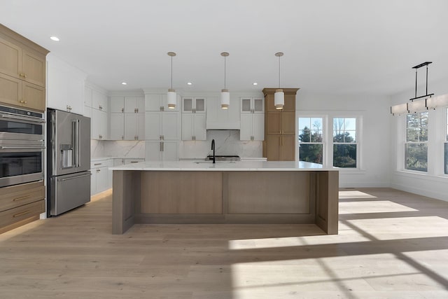 kitchen with tasteful backsplash, a large island with sink, appliances with stainless steel finishes, white cabinets, and light wood-type flooring