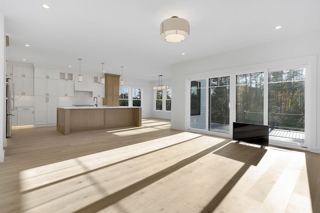 unfurnished living room with light hardwood / wood-style flooring, a notable chandelier, and sink