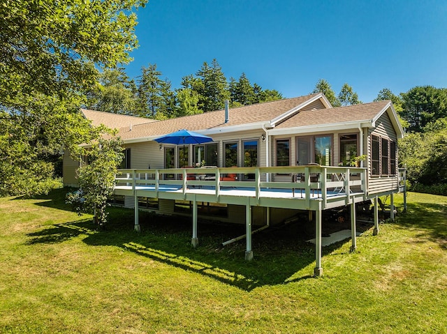 rear view of property featuring a sunroom, roof with shingles, a lawn, and a wooden deck