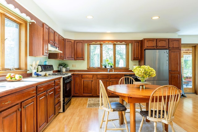 kitchen with under cabinet range hood, light countertops, range with gas cooktop, light wood finished floors, and stainless steel fridge