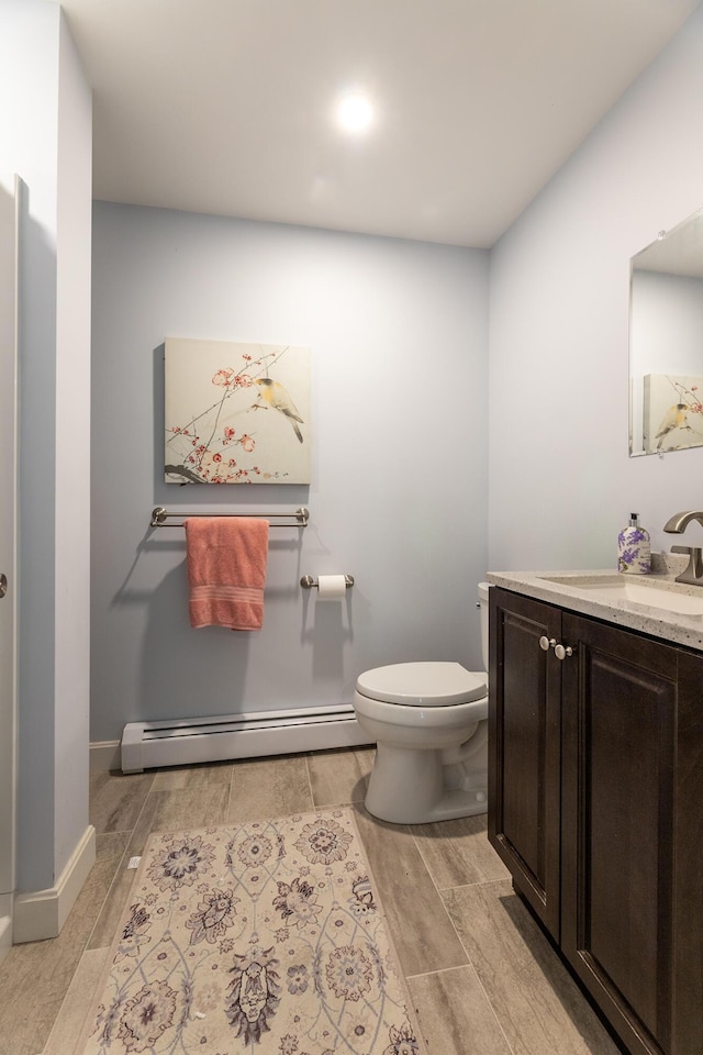 half bathroom with a baseboard radiator, toilet, vanity, baseboards, and wood tiled floor