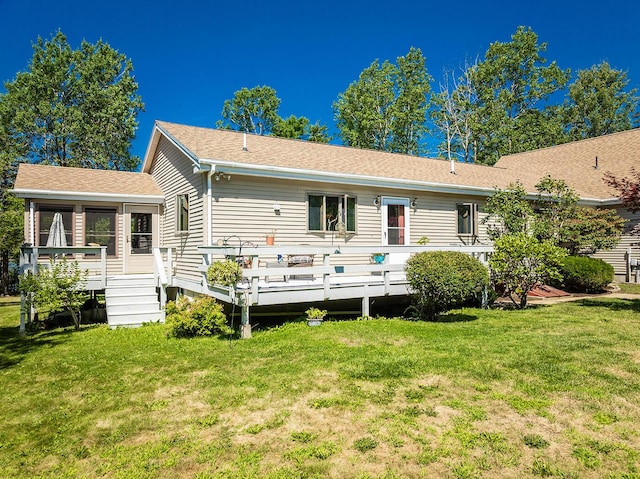 back of property with a deck, a yard, roof with shingles, and a sunroom