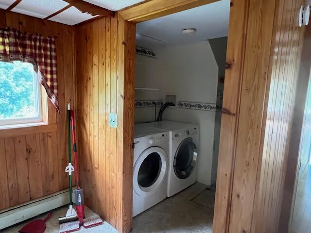 clothes washing area with washing machine and clothes dryer, wood walls, and a baseboard heating unit