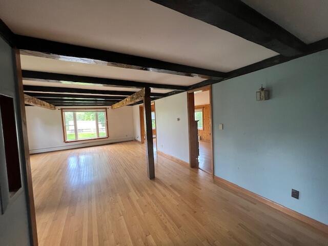 unfurnished room with beamed ceiling and light wood-type flooring