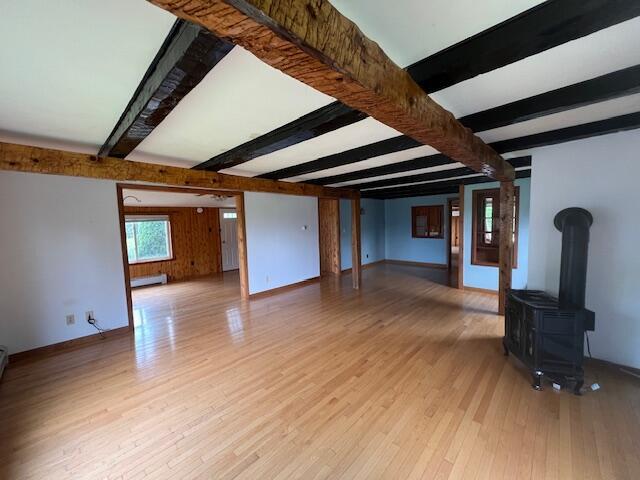 unfurnished living room with a wood stove, light hardwood / wood-style flooring, baseboard heating, and beam ceiling