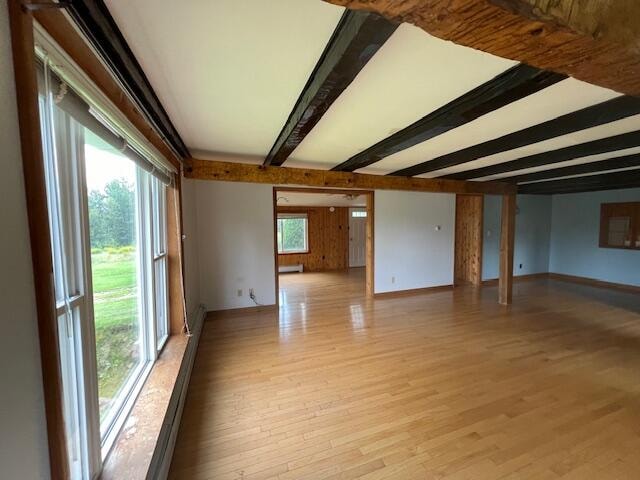 empty room with beam ceiling, light hardwood / wood-style flooring, and a wealth of natural light