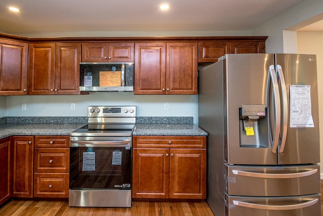 kitchen with light hardwood / wood-style floors, stainless steel appliances, and dark stone counters