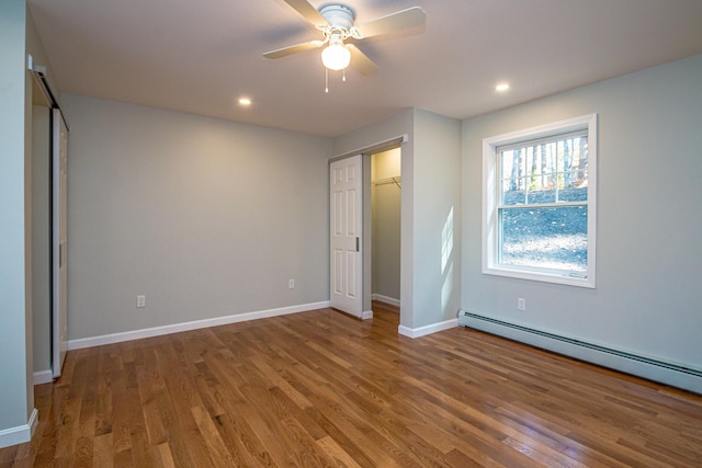 unfurnished bedroom featuring a closet, ceiling fan, hardwood / wood-style flooring, and a baseboard heating unit