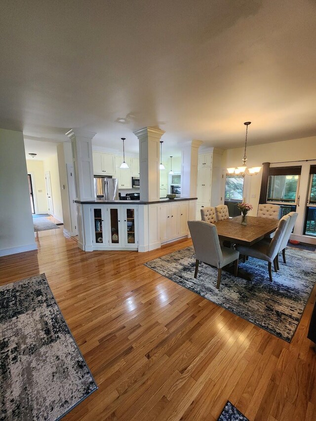 dining room with an inviting chandelier, decorative columns, and light wood-type flooring