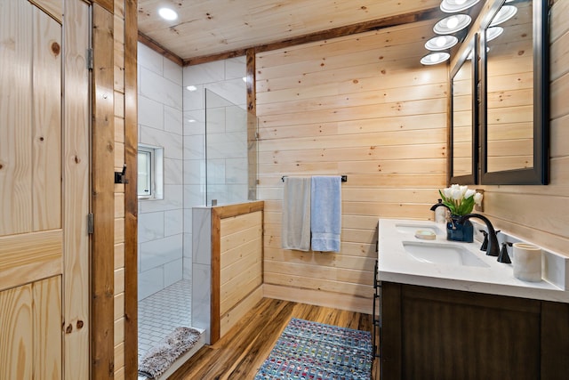 bathroom with wooden walls, hardwood / wood-style floors, wood ceiling, tiled shower, and vanity