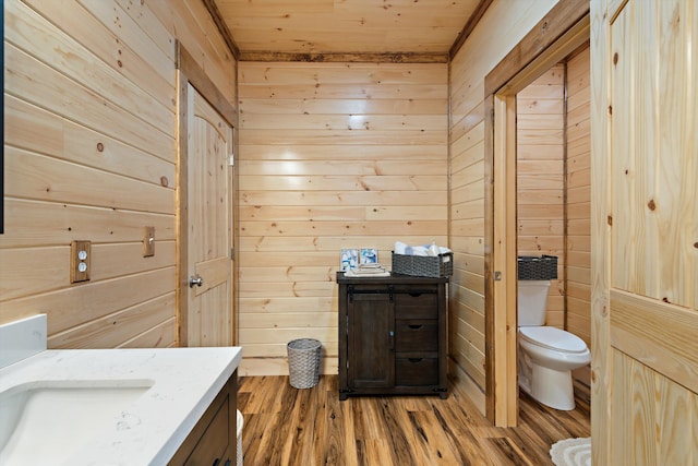 bathroom featuring wood-type flooring, wood walls, toilet, and vanity