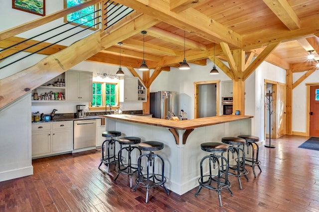 kitchen with appliances with stainless steel finishes, butcher block countertops, decorative light fixtures, white cabinetry, and a kitchen bar