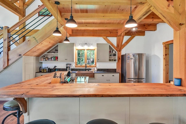 kitchen featuring pendant lighting, wood counters, stainless steel refrigerator, sink, and a kitchen bar