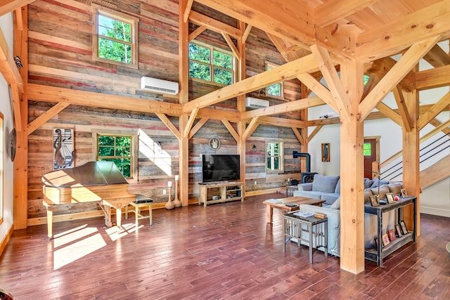 living room with an AC wall unit, a towering ceiling, wood walls, a wood stove, and dark wood-type flooring