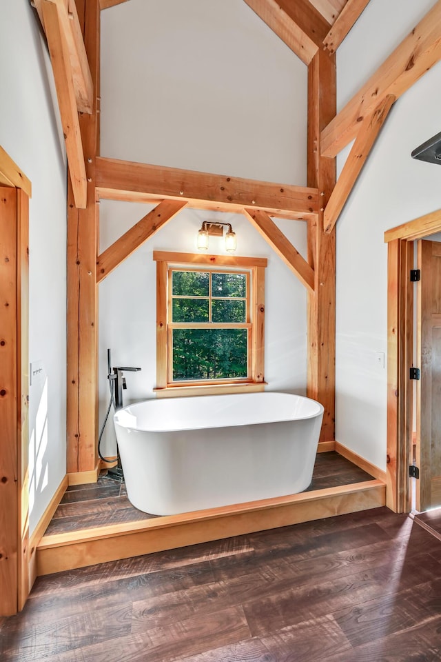 bathroom featuring wood-type flooring, high vaulted ceiling, and a tub to relax in