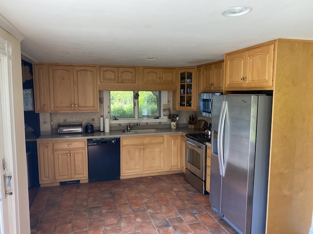 kitchen featuring appliances with stainless steel finishes, glass insert cabinets, a sink, backsplash, and light brown cabinetry