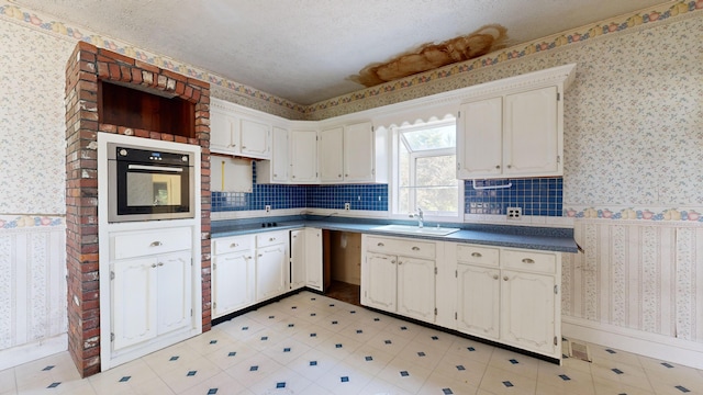 kitchen featuring sink, a textured ceiling, white cabinets, and stainless steel oven