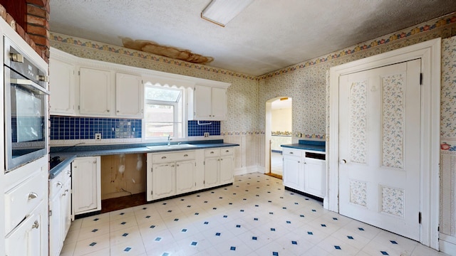 kitchen with stainless steel oven, sink, a textured ceiling, and white cabinets