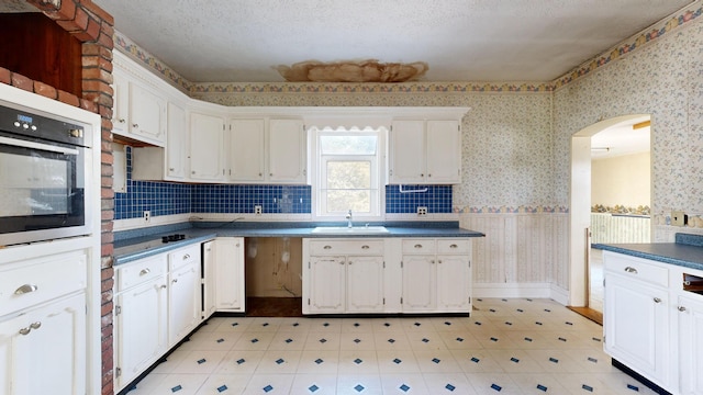 kitchen featuring oven, sink, a textured ceiling, and white cabinets