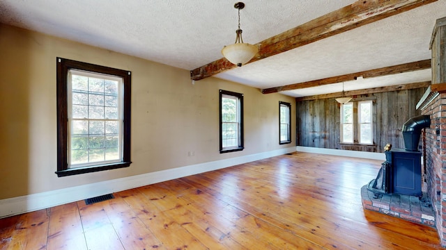 unfurnished living room with beamed ceiling, a healthy amount of sunlight, hardwood / wood-style flooring, and a wood stove