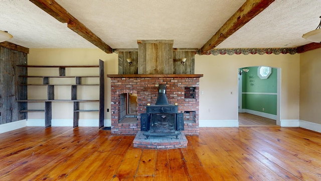 unfurnished living room with hardwood / wood-style floors, beam ceiling, a textured ceiling, and a wood stove