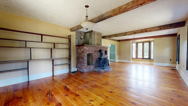 unfurnished living room featuring beam ceiling, wood-type flooring, a textured ceiling, and a wood stove