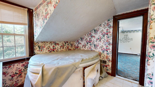 bedroom featuring vaulted ceiling, light tile patterned floors, and a textured ceiling