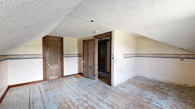 additional living space featuring vaulted ceiling, a textured ceiling, and light hardwood / wood-style floors