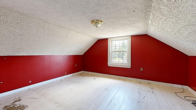 additional living space featuring vaulted ceiling, a textured ceiling, and light wood-type flooring