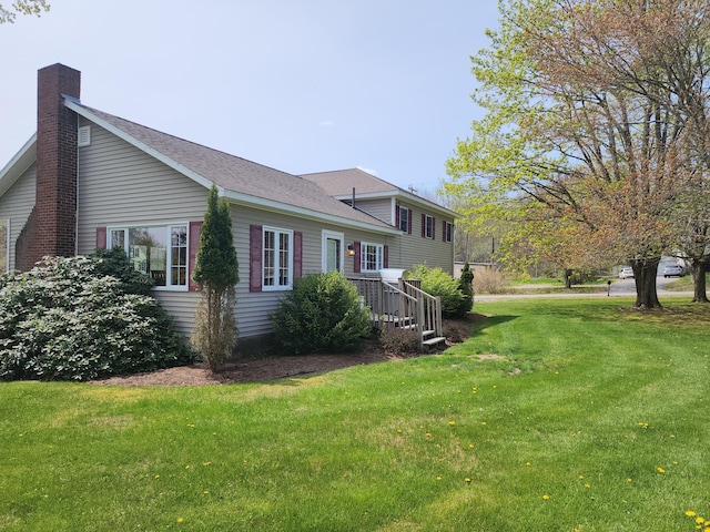 rear view of property with a chimney, roof with shingles, and a lawn