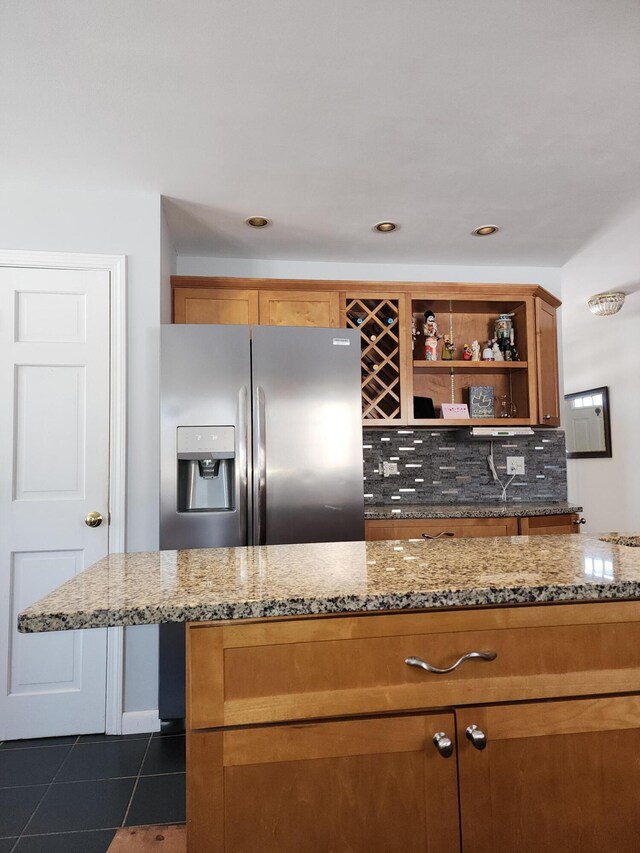 kitchen featuring backsplash, light stone counters, dark tile patterned flooring, and stainless steel fridge