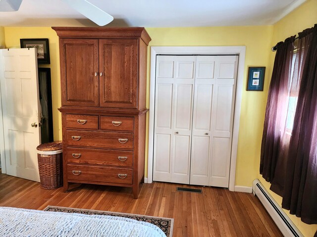 bedroom with a closet, wood-type flooring, a baseboard radiator, and ceiling fan