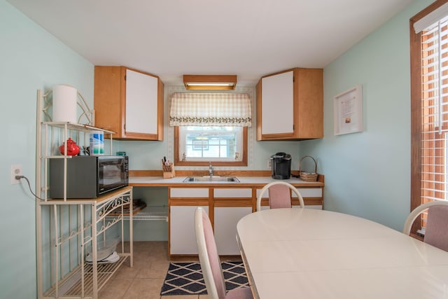 kitchen featuring light tile patterned floors, black microwave, light countertops, and a sink