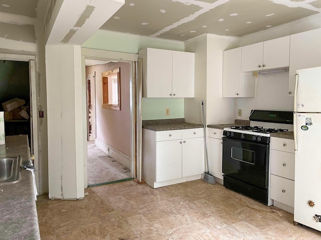 kitchen with dark countertops, freestanding refrigerator, black range with gas stovetop, white cabinetry, and a sink