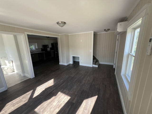 unfurnished living room featuring dark wood-type flooring, ornamental molding, and an AC wall unit