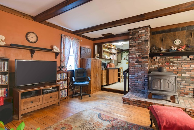 living room with beam ceiling, light hardwood / wood-style flooring, and a wood stove