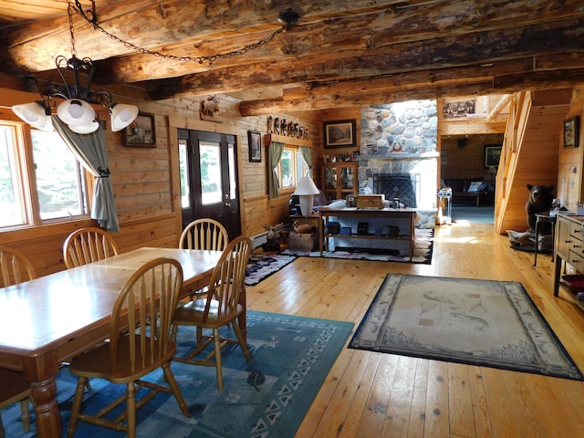 dining area featuring beam ceiling, a stone fireplace, plenty of natural light, and light hardwood / wood-style floors