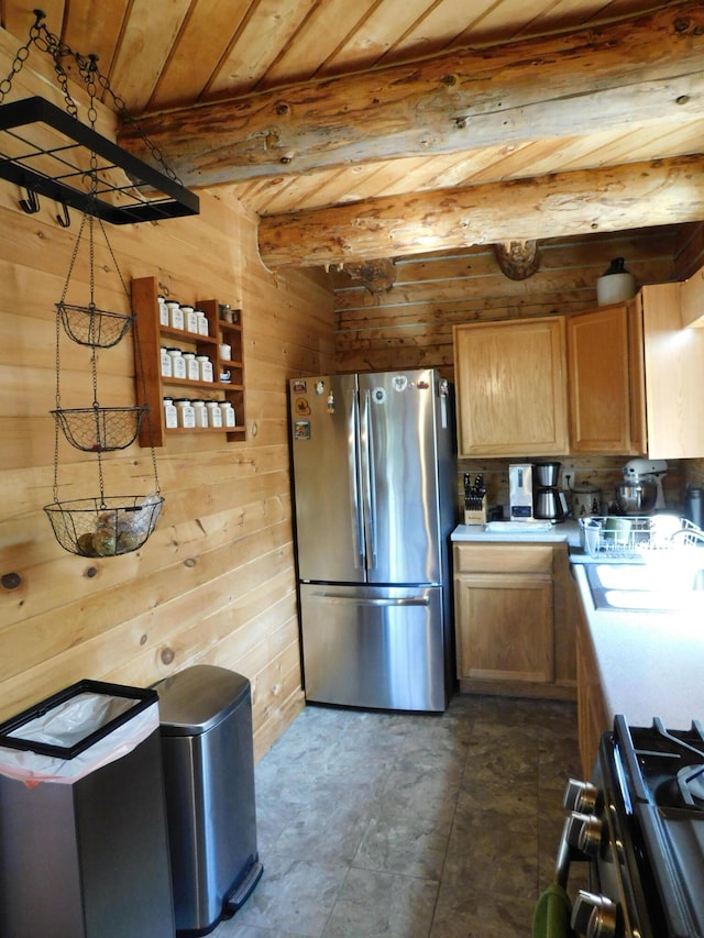 kitchen with tile patterned floors, wooden walls, stainless steel refrigerator, beam ceiling, and sink