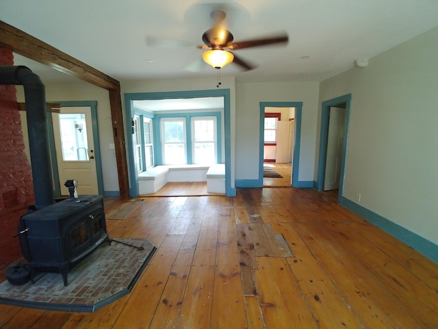 unfurnished living room with ceiling fan, a wood stove, and wood-type flooring