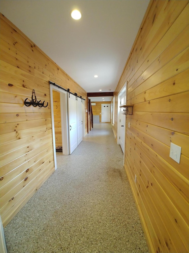 corridor with a barn door, wood walls, and crown molding