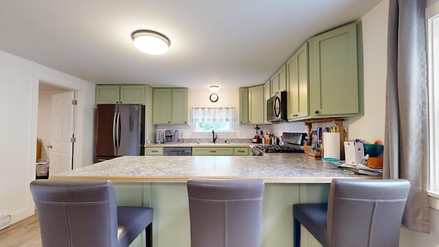 kitchen featuring light wood-type flooring, appliances with stainless steel finishes, kitchen peninsula, and a kitchen breakfast bar