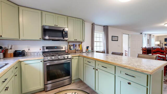 kitchen featuring light wood-type flooring, green cabinets, kitchen peninsula, and stainless steel appliances