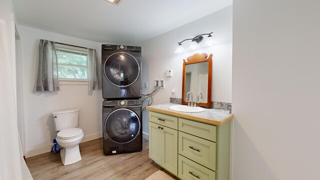 bathroom with stacked washer and clothes dryer, toilet, hardwood / wood-style floors, and vanity