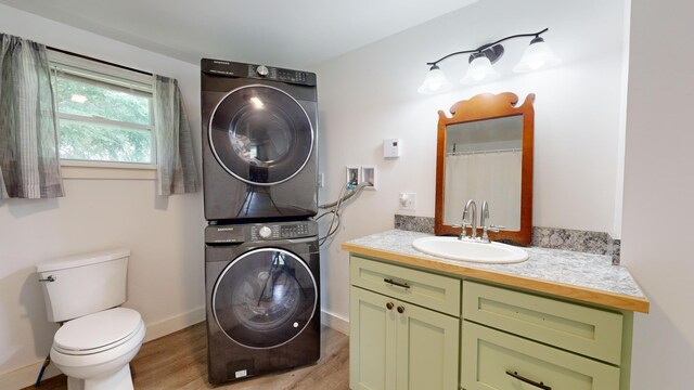 bathroom featuring wood-type flooring, toilet, stacked washer and clothes dryer, and vanity