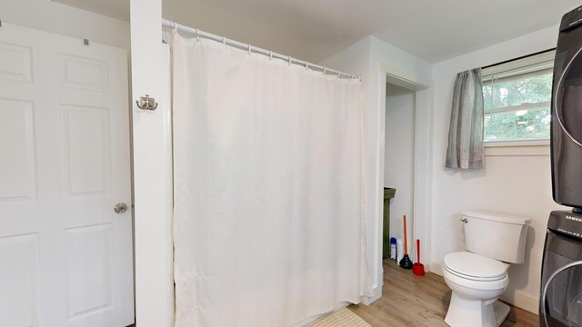 bathroom featuring toilet, wood-type flooring, and stacked washing maching and dryer