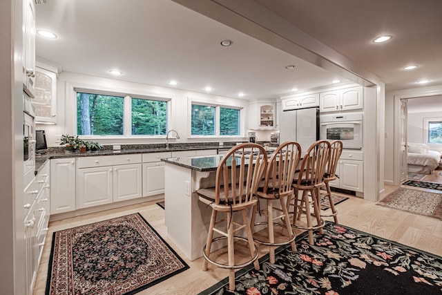 kitchen featuring light hardwood / wood-style floors, a healthy amount of sunlight, white cabinets, white oven, and stainless steel refrigerator